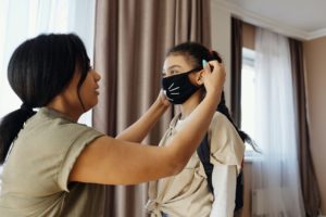 A mother puts on a mask for her daughter before she goes to school.