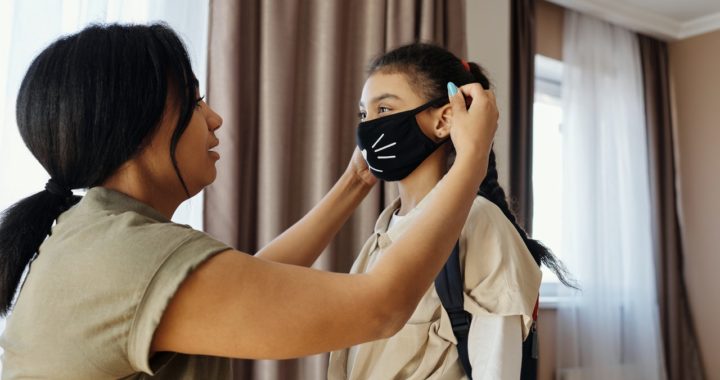 A mother puts on a mask for her daughter before she goes to school.